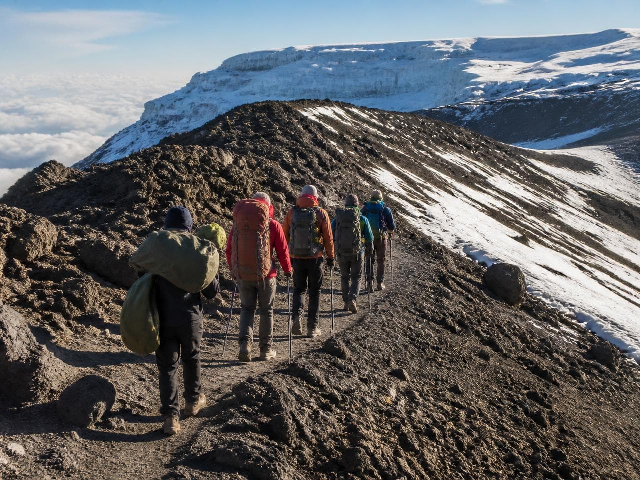 Line of trekkers walking a rocky ridge towards snow on Kilimanjaro